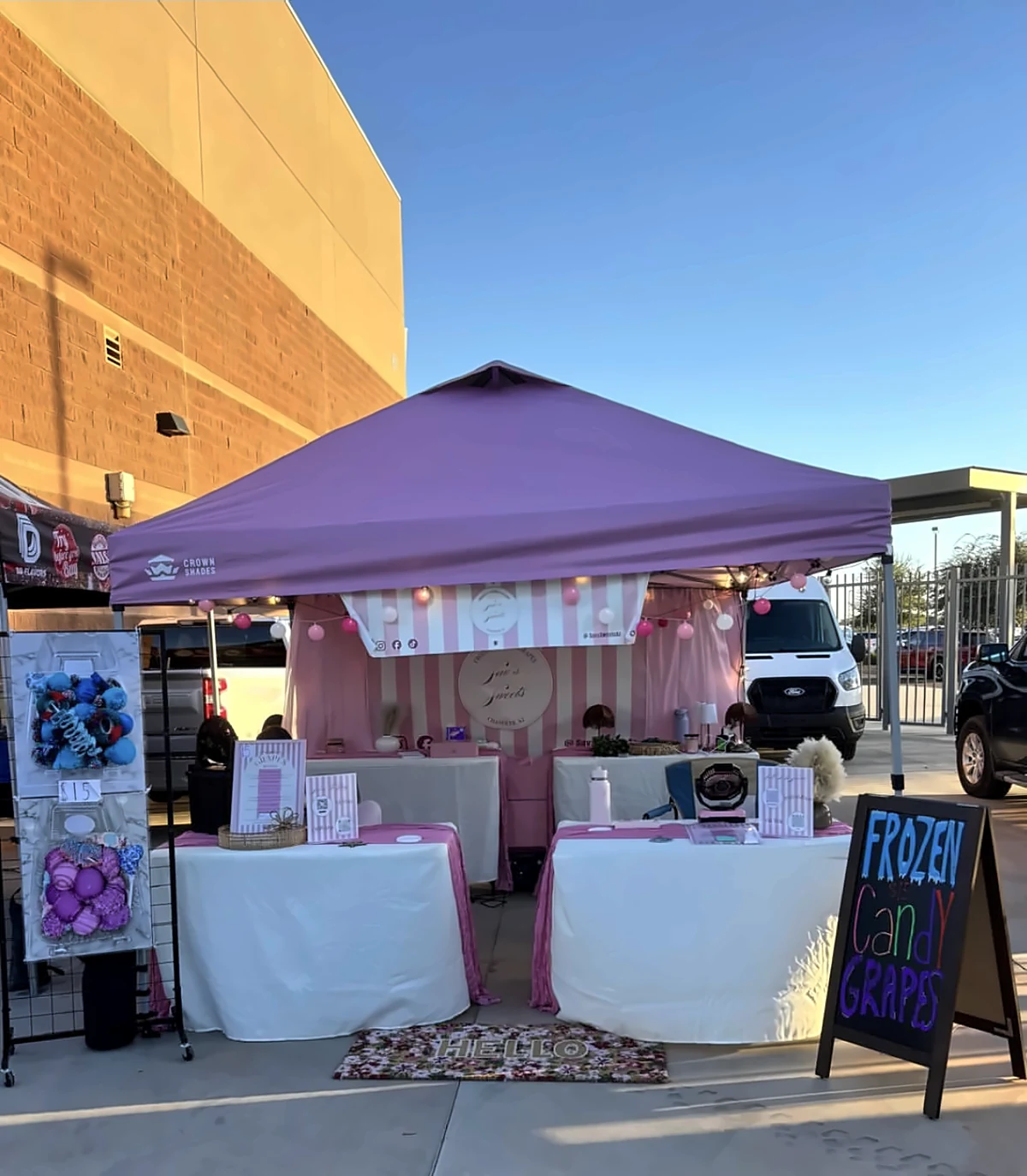 Sav's Sweets booth with a lilac tent, pink striped backdrop and a Frozen Candy Grapes chalkboard sign